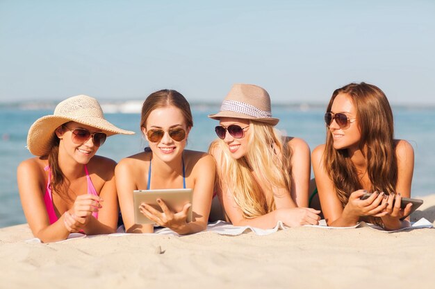 vacanze estive, viaggi, tecnologia e concetto di persone - gruppo di donne sorridenti in occhiali da sole con computer tablet pc sdraiati sulla spiaggia