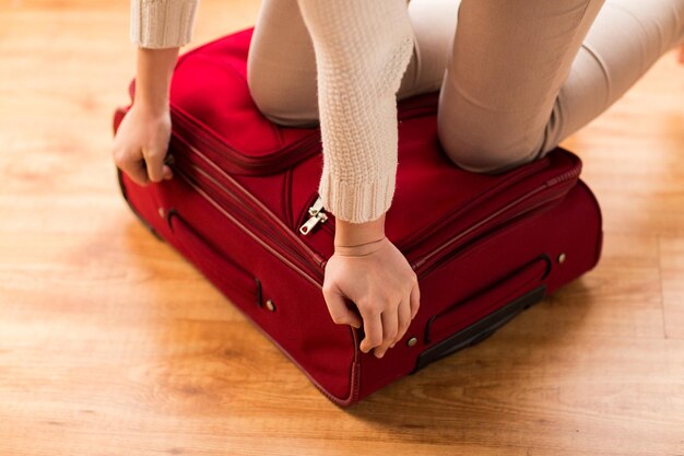 vacanze estive, viaggi, turismo e concetto di oggetti - primo piano della donna che fa i bagagli e chiude la borsa da viaggio per le vacanze
