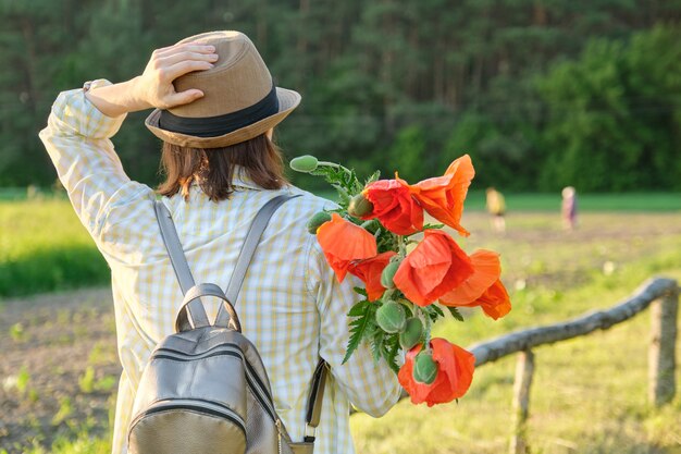 Vacanze estive, viaggio nella natura, bella donna matura che cammina lungo la strada di campagna con i papaveri