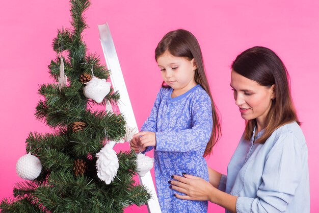 Vacanze famiglia e concetto di natale madre e figlia che decorano l'albero di natale in rosa