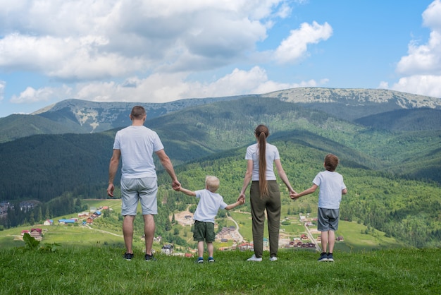 Vacanze in famiglia. Genitori e due figli ammirano la vista sulla valle. Montagne in lontananza. Vista posteriore