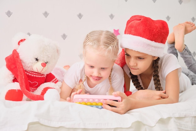 Vacanze invernali e concetto di bambini - ragazze sorridenti felici con lo smartphone sdraiato sulle luci di natale del letto