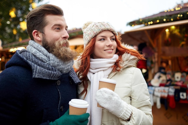 vacanze, inverno, natale, bevande calde e concetto di persone - coppia felice di turisti in abiti caldi che bevono caffè da bicchieri di carta usa e getta nella città vecchia