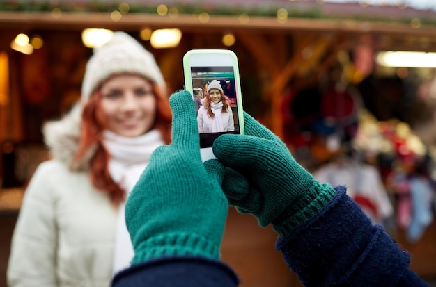 vacanze, inverno, natale, tecnologia e concetto di persone - coppia felice di turisti in abiti caldi che scattano foto con lo smartphone nella città vecchia