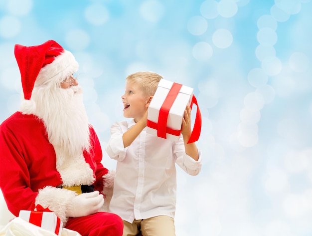 vacanze, natale, infanzia e concetto di persone - ragazzino sorridente con babbo natale e regali su sfondo di luci blu