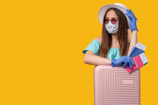 Vacanze pandemiche Viaggio estivo Donna turistica in maschera protettiva guanti con valigia pronta per il viaggio isolata su spazio vuoto arancione Restrizione pandemica del coronavirus Distanziamento sociale Nuova normalità