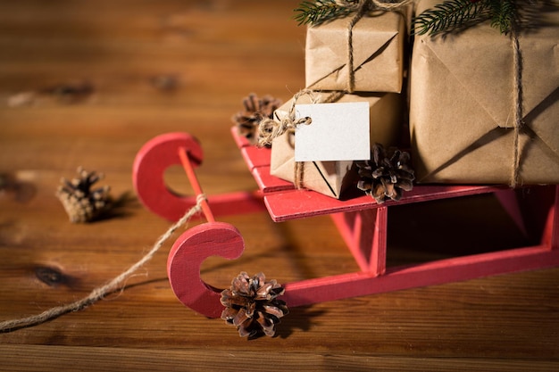 vacanze, regali, capodanno e concetto di celebrazione - primo piano di scatole regalo con nota vuota su slitta di legno rossa e pigne