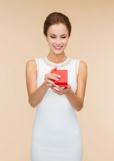 vacanze, regali, matrimonio e concetto di felicità - donna sorridente in abito bianco con scatola regalo rossa su sfondo beige