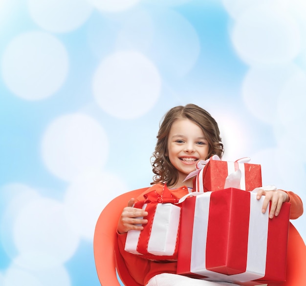 vacanze, regali, natale, infanzia e concetto di persone - bambina sorridente con scatole regalo su sfondo di luci blu