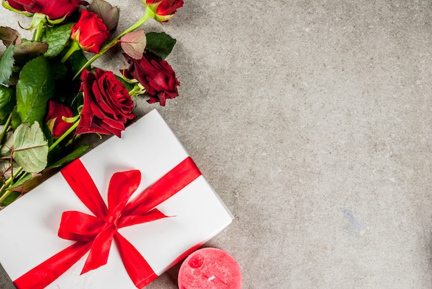 Vacanze, San Valentino. Bouquet di rose rosse, cravatta con un nastro rosso, con confezione regalo avvolta e candela rossa. Su un tavolo di pietra grigia, copyspace vista dall'alto