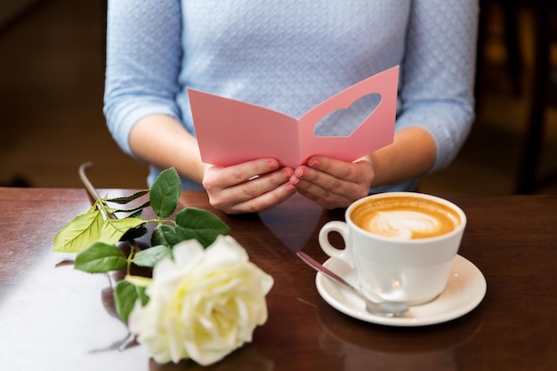 vacanze, san valentino, persone e concetto di amore - primo piano della donna che legge il biglietto di auguri con cuore, fiore e caffè