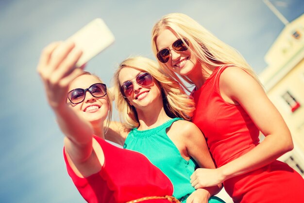 vacanze, turismo e concetto di tecnologia moderna - ragazze sorridenti che scattano foto con la fotocamera dello smartphone in città