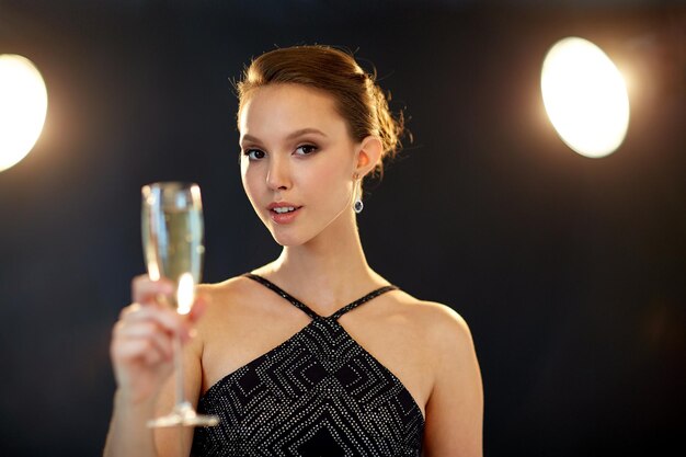 vacanze, vita notturna, bevande, persone e concetto di lusso - bella giovane donna sorridente asiatica che beve champagne alla festa su sfondo nero e faretti