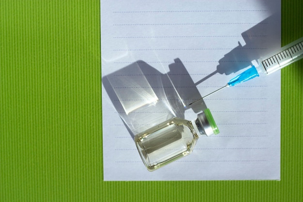 Vaccinazione globale La bottiglia di medicina e la siringa con una grande ombra sono sulla nota vuota sul verde