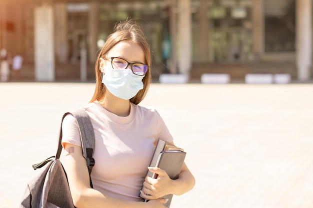 Vaccinazione nelle università e nei collegeStudenti vaccinati tornano a scuola dopo la pandemia di covid19 su una ragazza adolescente con una maschera medica con cerotto a portata di mano accanto all'università