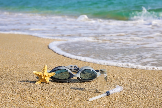 Vaccino contro Covid-19, siringa, occhiali da sub e stelle marine sulla spiaggia.