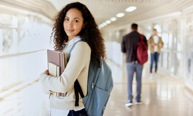 Vado in classe Ritratto ritagliato di una giovane studentessa universitaria attraente in piedi con i suoi libri di testo in un corridoio del campus