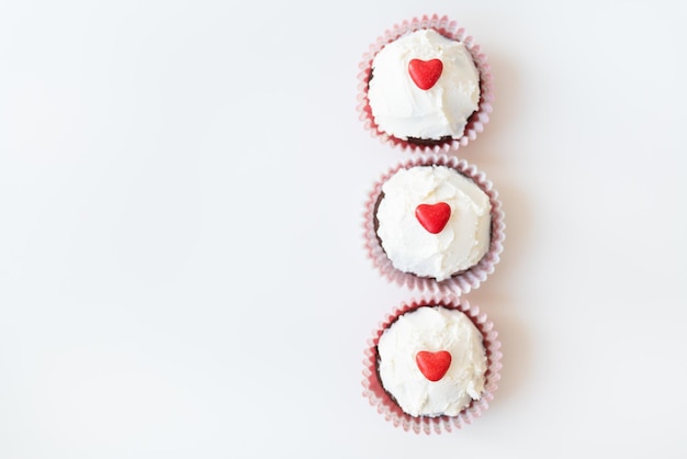 Valentine14 febbraio Muffin dolci al cioccolato con crema al burro e un cuore rosso per la decorazione su fondo bianco