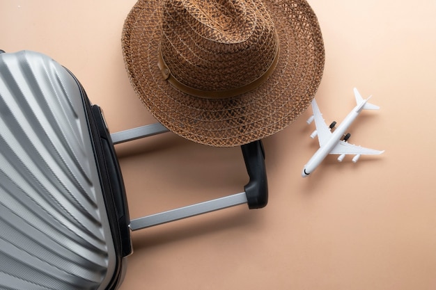 Valigia grigia piatta con cappello marrone e mini aereo