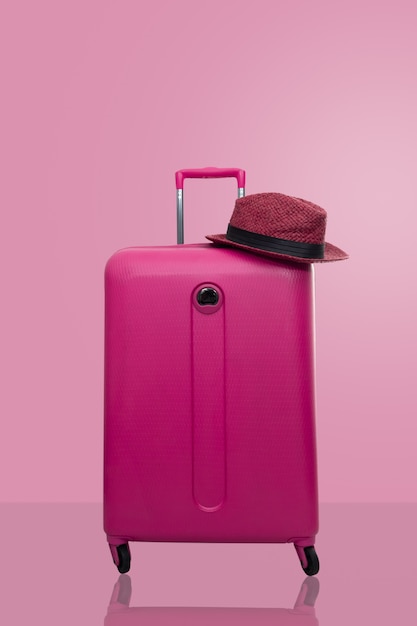 Valigia rosa con cappello su sfondo rosa pastello. concetto di viaggio.