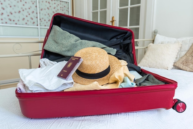 Valigia rosa sul letto con vestiti, cappello estivo e passaporto rumeno pronto per il viaggio.