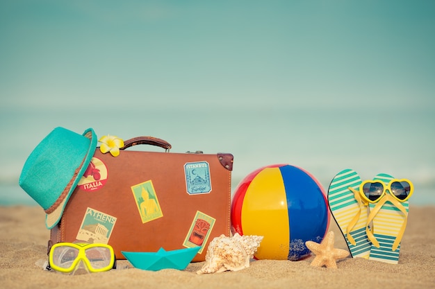 Valigia vintage e infradito sulla spiaggia sabbiosa contro il mare e il cielo blu