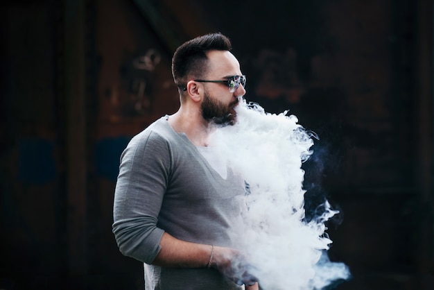 Vaper con la barba in occhiali da sole vaping all&#39;aperto