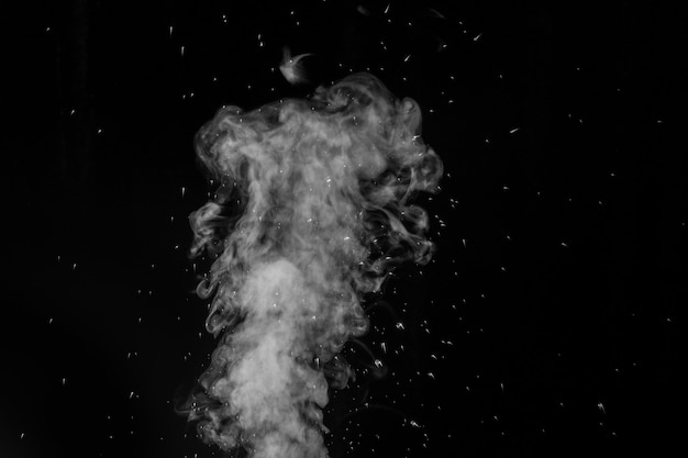 Vapore bianco riccio che sale e spruzzi d'acqua che si disperdono in direzioni diverse isolate su una parete nera. Evaporazione di liquidi e condensa.