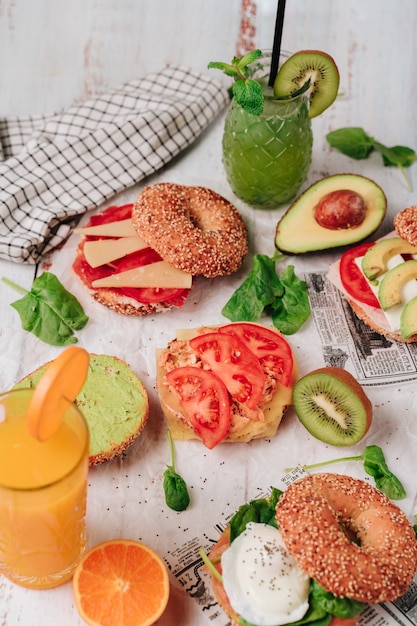 Vari bagel su un tavolo Sono fatti con sesamo e pane di chia pomodoro prosciutto iberico pollo formaggio avocado guacamole e salmone Da bere ci sono kiwi e succhi d'arancia