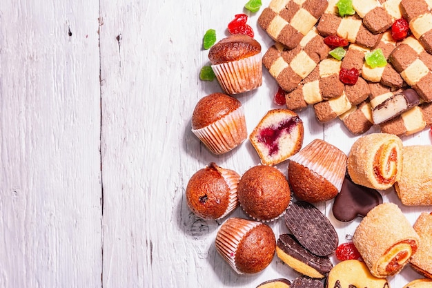 Vari biscotti e cupcakes assortiti. Luce dura alla moda, ombra scura. Sfondo di tavole di legno bianche, vista dall'alto