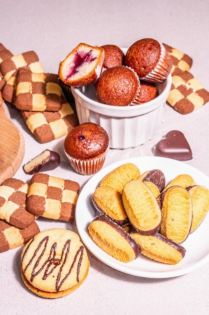 Vari biscotti e muffin assortiti. Luce dura alla moda, ombra scura. Sfondo di pietra concreta, primo piano