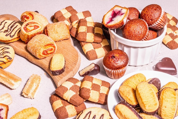 Vari biscotti e muffin assortiti. Luce dura alla moda, ombra scura. Sfondo di pietra concreta, primo piano