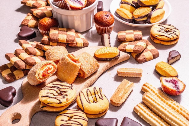 Vari biscotti e muffin assortiti. Luce dura alla moda, ombra scura. Sfondo di pietra concreta, primo piano