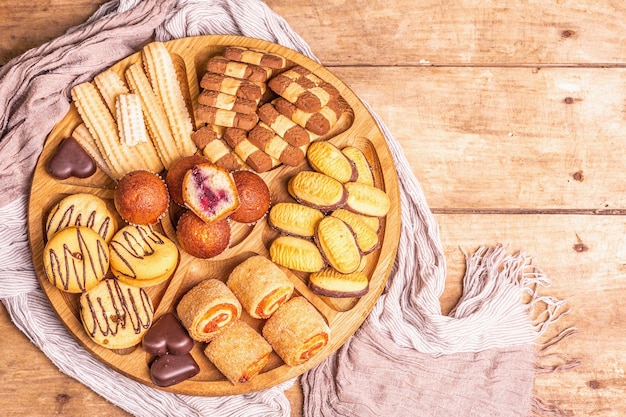 Vari biscotti e muffin assortiti. Piastra combinata in legno su tavola di vecchie tavole, vista dall'alto