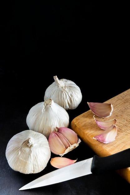 Vari garlics e anche spicchi d'aglio su un tagliere di legno accanto a un coltello da cucina isolato ag