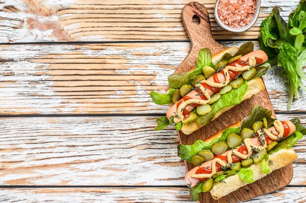 Vari hot dog con verdure, lattuga e condimenti. Fondo in legno bianco. Vista dall'alto. Copia spazio.