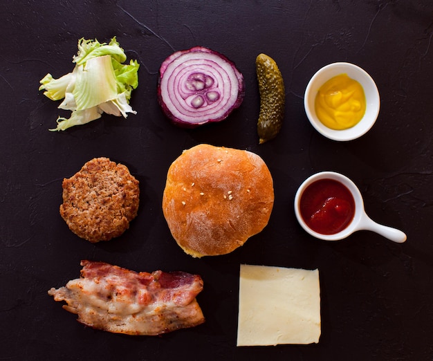 Vari prodotti alimentari isolati su sfondo nero Ingredienti principali di gustoso cheeseburger Idee per cucinare a casa varianti dei pasti preferiti di fast food