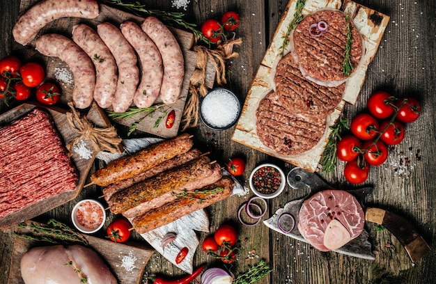 Vari tipi di carne cruda alla griglia e barbecue Salsicce di bistecca di pollo carne di manzo macinata spiedini di maiale con spezie alle erbe su sfondo di legno Formato banner lungo vista dall'alto