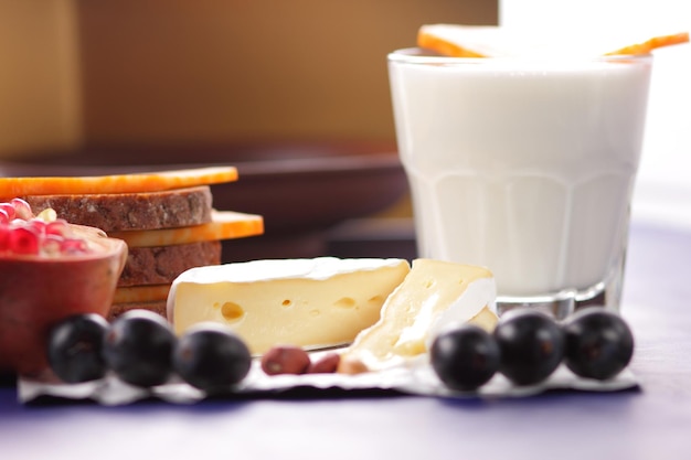 Vari tipi di composizione di formaggio su sfondo blu closeup Formaggi con frutta secca e un bicchiere di latte su carta pergamena