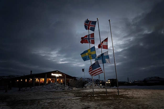 Varie bandiere dei paesi nordici stanno sventolando sull'asta della bandiera nel vento sullo sfondo del cielo notturno tra le nuvole. Paesaggio drammatico