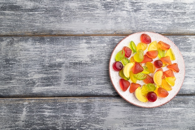 Varie caramelle di gelatina di frutta sulla piastra su fondo di legno grigio