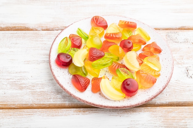 Varie caramelle di gelatina di frutta sulla zolla su fondo di legno bianco.