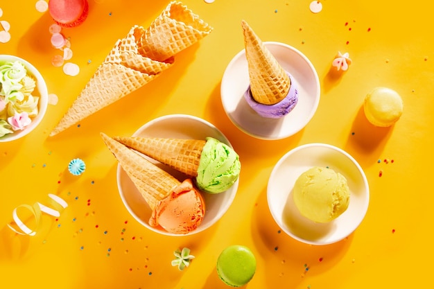 Varie palline o palline di gelato colorate con coni di cialda su sfondo giallo Vista dall'alto