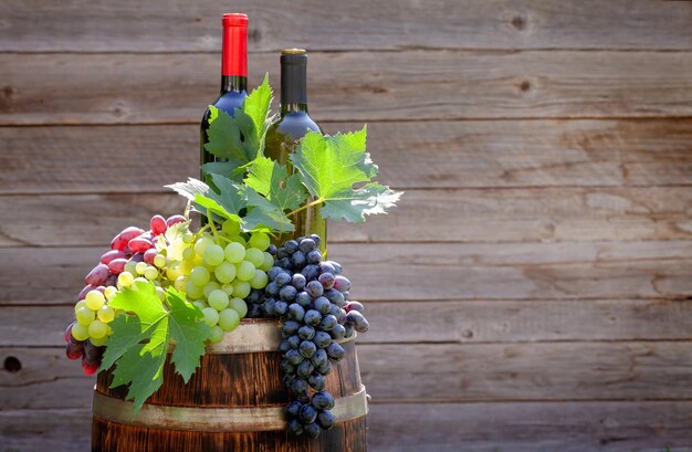 Varie uve colorate e bottiglie di vino sulla botte di vino