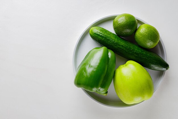 Varie verdure verdi e frutta su un piatto bianco. Mela verde, cetriolo, peperone dolce e lime su un tavolo bianco. Copia spazio. Lay piatto