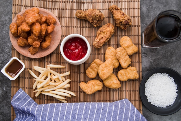 Varietà di cibi di pollo con patatine fritte e bibita sulla stuoia di bambù