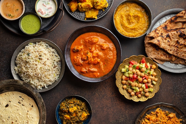 Varietà di cibo indiano, piatti diversi e snack su sfondo rustico scuro. Pilaf, pollo al curry, riso, palak paneer, pollo tikka, zuppa dal, pane naan, assortimento di chutney. Vista dall'alto