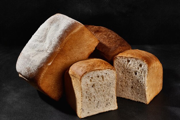 Varietà di gustoso pane cotto intero e tagliato a metà cosparso di farina su sfondo nero copia spac