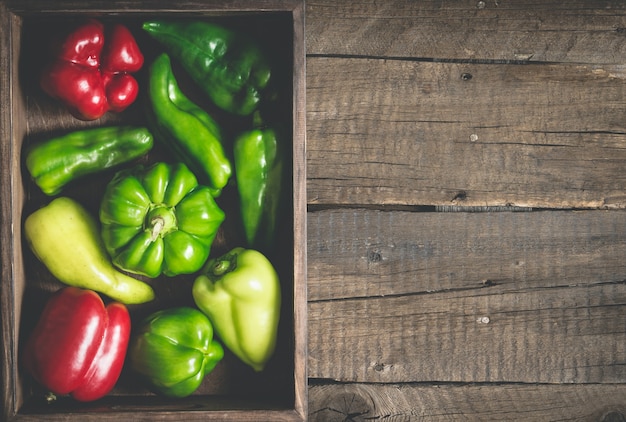 Varietà di peperoni rossi e verdi di varie forme. Vassoio di verdure completo su fondo in legno.