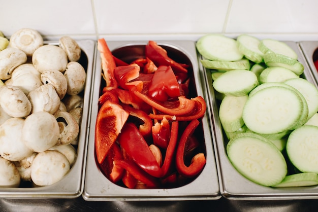 Varietà di verdure affettate preparate per la cottura in una cucina professionale, come funghi, peperoni, zucchine